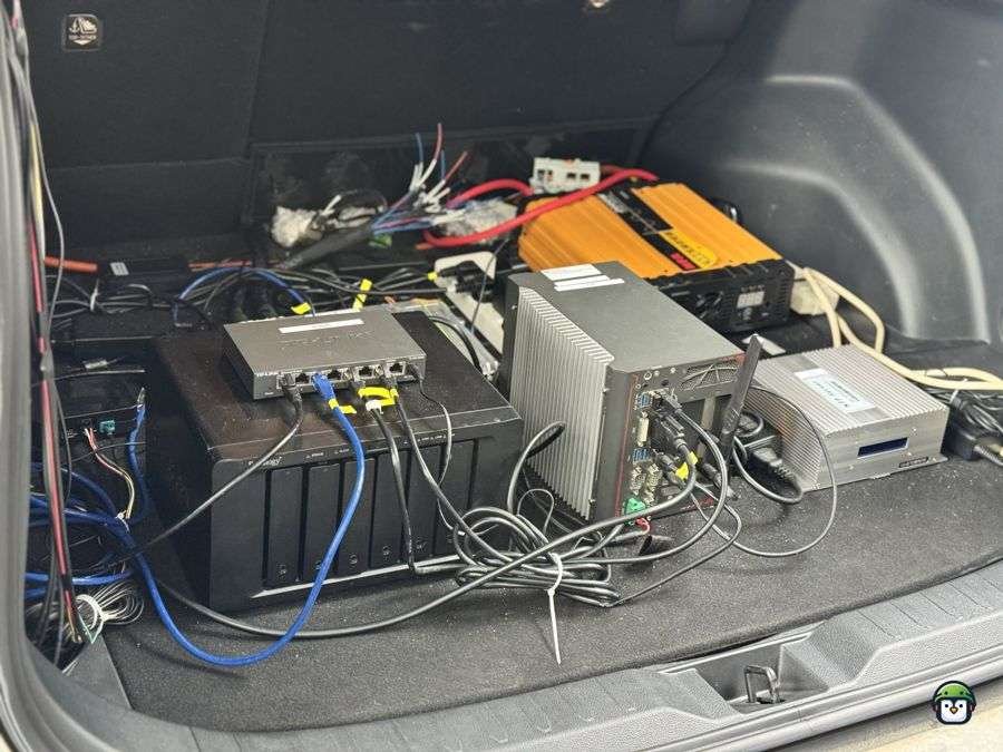 Seized equipment includes an orange power inverter, a silver mini-PC with an antenna, a gray storage device, a black Synology NAS server with multiple drive bays, a black TP-Link network switch with multiple Ethernet ports, and various power and Ethernet cables laid out on a table.